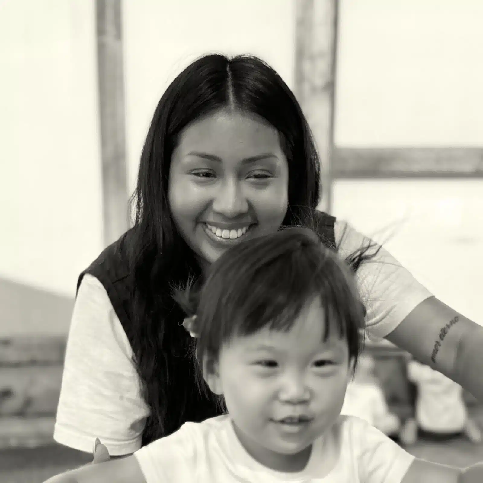 Smiling Asian woman with long dark hair holding a young child indoors, both smiling in a candid moment.